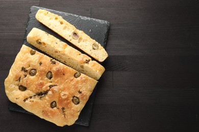 Photo of Pieces of delicious focaccia bread with olives and thyme on dark wooden table, top view. Space for text