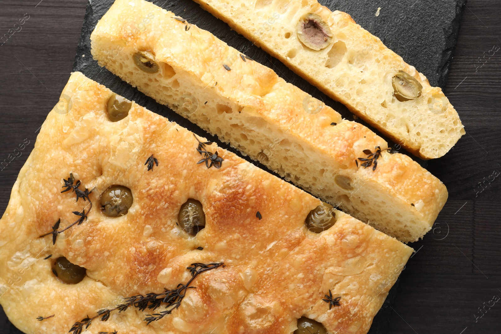 Photo of Pieces of delicious focaccia bread with olives and thyme on dark wooden table, top view