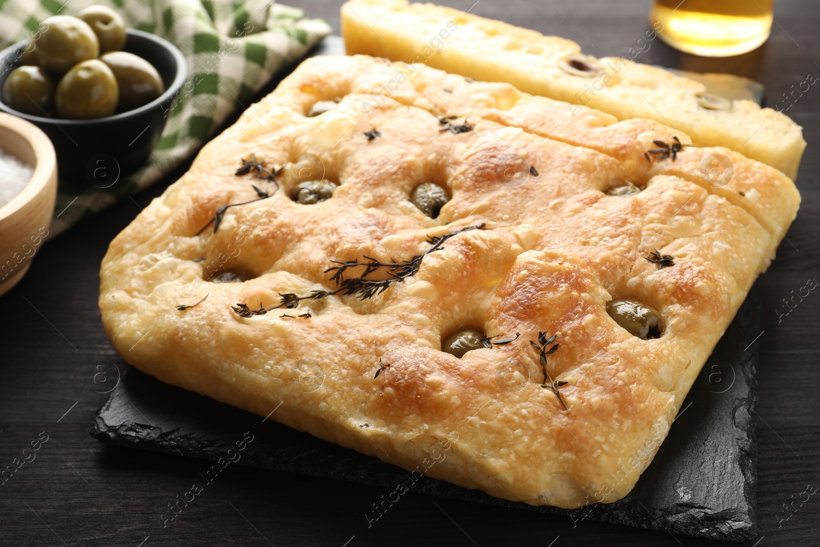 Photo of Pieces of delicious focaccia bread with olives and thyme on dark wooden table, closeup