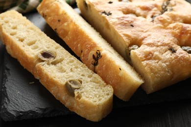 Photo of Pieces of delicious focaccia bread with olives and thyme on table, closeup