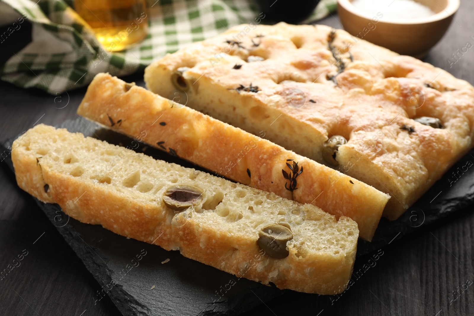 Photo of Pieces of delicious focaccia bread with olives and thyme on dark wooden table, closeup