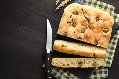 Photo of Pieces of delicious focaccia bread with olives, thyme, spikes and knife on dark wooden table, flat lay. Space for text