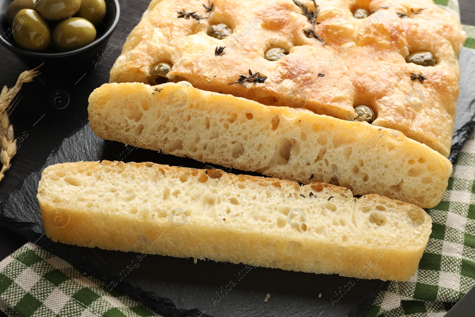 Photo of Pieces of delicious focaccia bread with olives and thyme on table, closeup