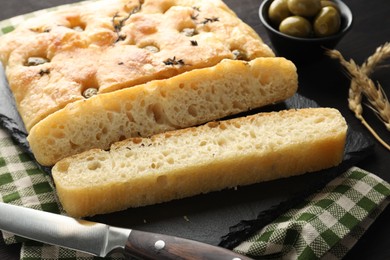 Photo of Pieces of delicious focaccia bread with olives, thyme, spikes and knife on table, closeup