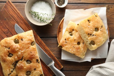 Photo of Pieces of delicious focaccia bread with olives, thyme, salt and knife on wooden table, flat lay