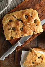 Photo of Pieces of delicious focaccia bread with olives, thyme, salt and knife on wooden table, flat lay