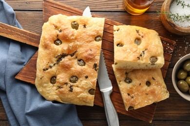 Photo of Pieces of delicious focaccia bread with olives, thyme, salt and knife on wooden table, flat lay