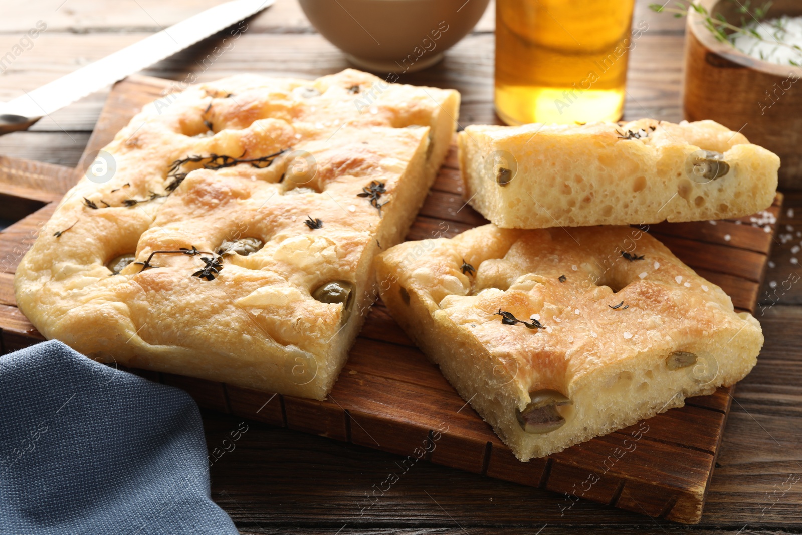 Photo of Pieces of delicious focaccia bread with olives, thyme and salt on wooden table, closeup