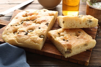 Photo of Pieces of delicious focaccia bread with olives, thyme and salt on wooden table, closeup