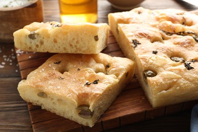 Photo of Pieces of delicious focaccia bread with olives, thyme and salt on wooden table, closeup