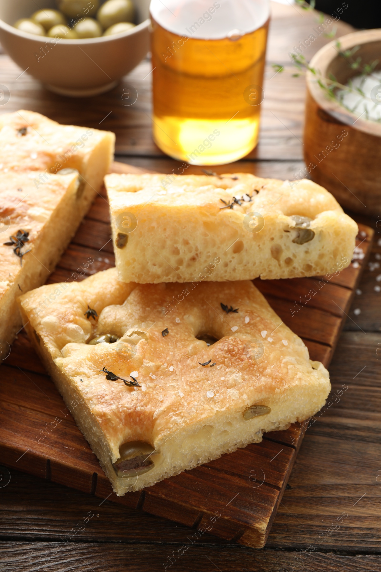 Photo of Pieces of delicious focaccia bread with olives, thyme, oil and salt on wooden table, closeup