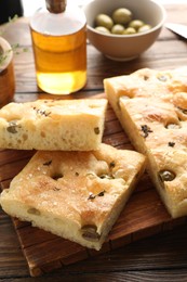 Photo of Pieces of delicious focaccia bread with olives, thyme, oil and salt on wooden table, closeup