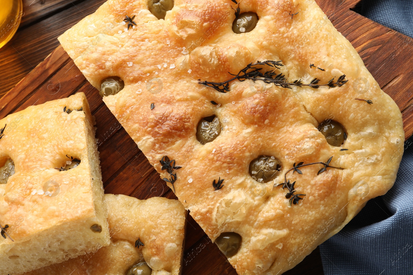 Photo of Pieces of delicious focaccia bread with olives and thyme on wooden table, top view