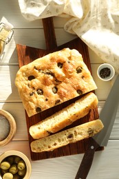 Photo of Pieces of delicious focaccia bread with olives, thyme, spices and knife on white wooden table, flat lay