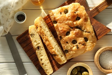 Photo of Pieces of delicious focaccia bread with olives, thyme, spices and knife on white wooden table, flat lay