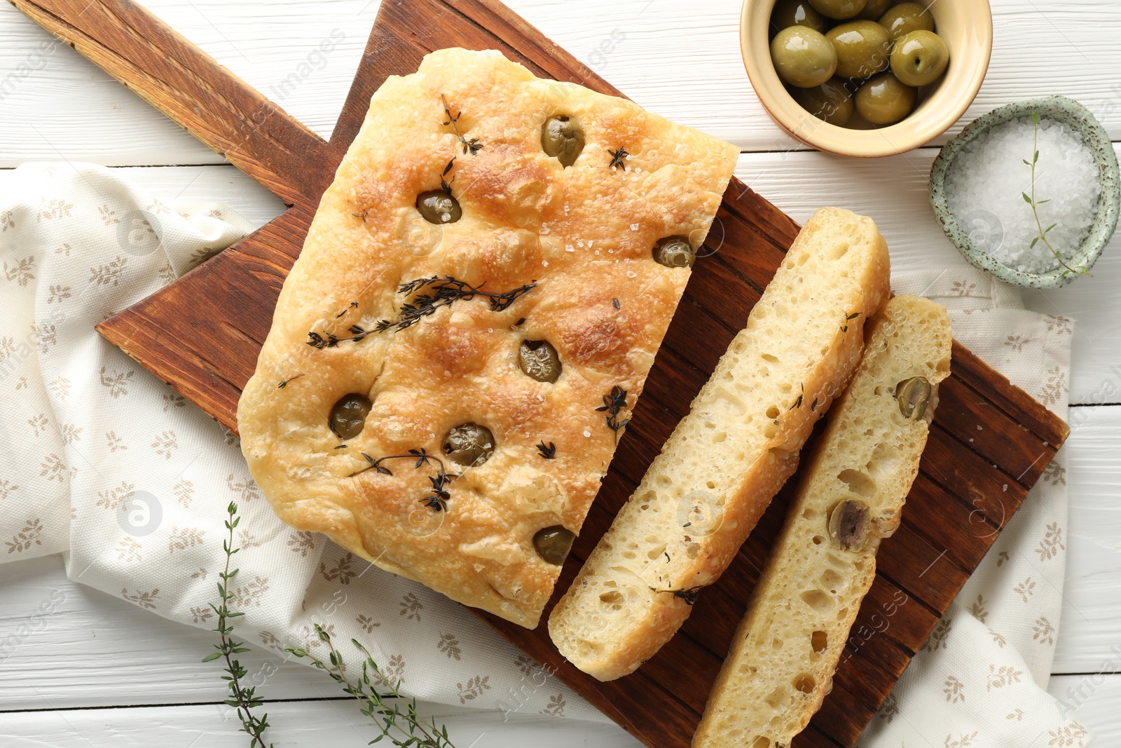 Photo of Pieces of delicious focaccia bread with olives, thyme and salt on white wooden table, flat lay