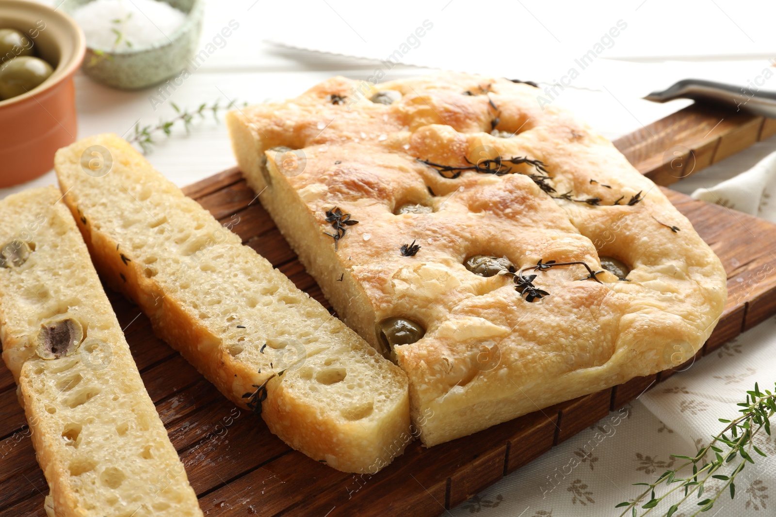 Photo of Pieces of delicious focaccia bread with olives, thyme and salt on table, closeup