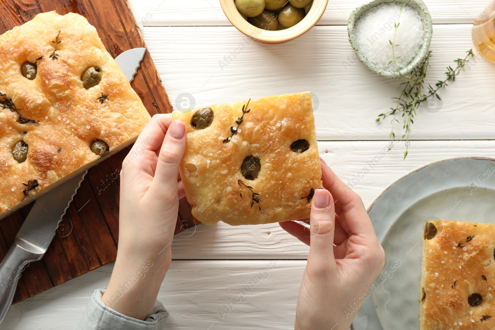 Photo of Woman with piece of delicious focaccia bread at white wooden table, top view