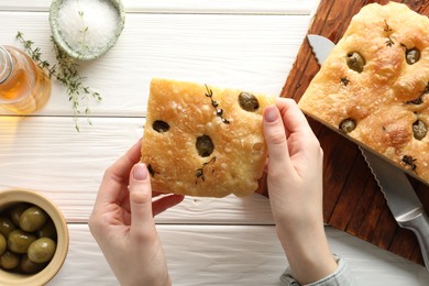 Photo of Woman with piece of delicious focaccia bread at white wooden table, top view