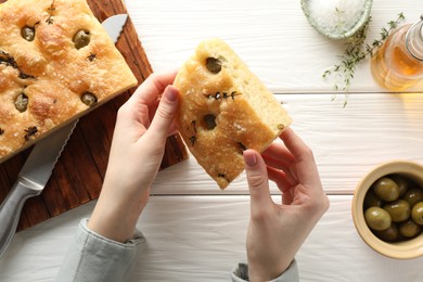 Photo of Woman with piece of delicious focaccia bread at white wooden table, top view