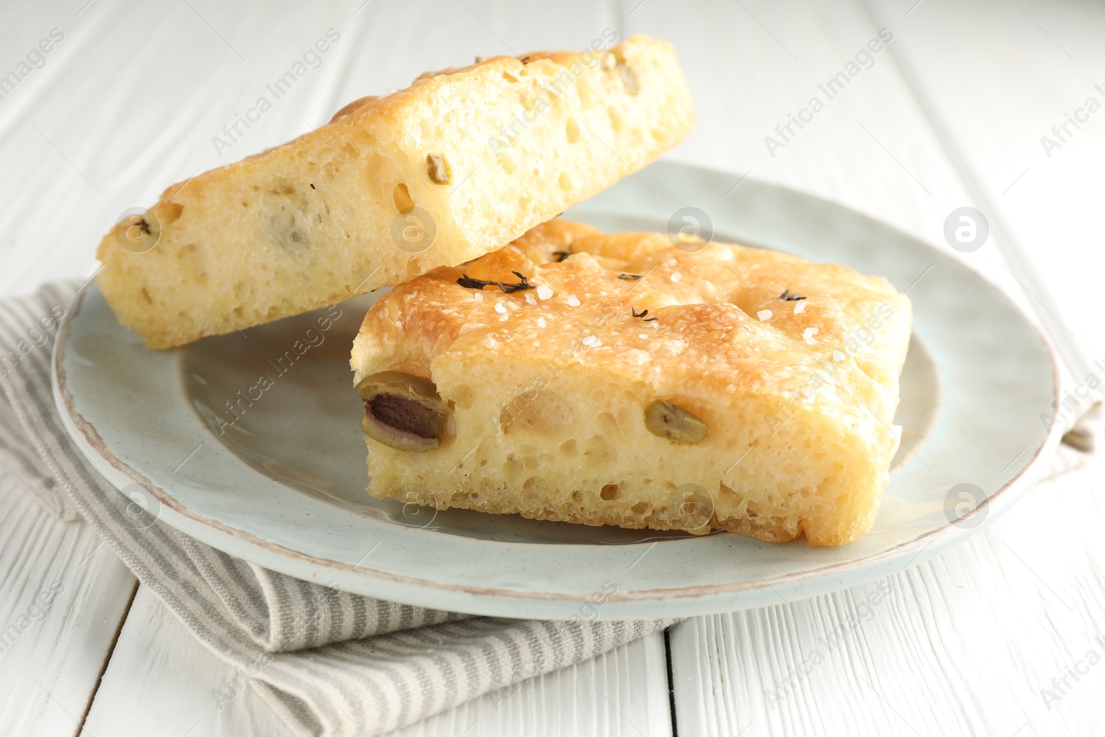 Photo of Pieces of delicious focaccia bread with olives, thyme and salt on white wooden table, closeup