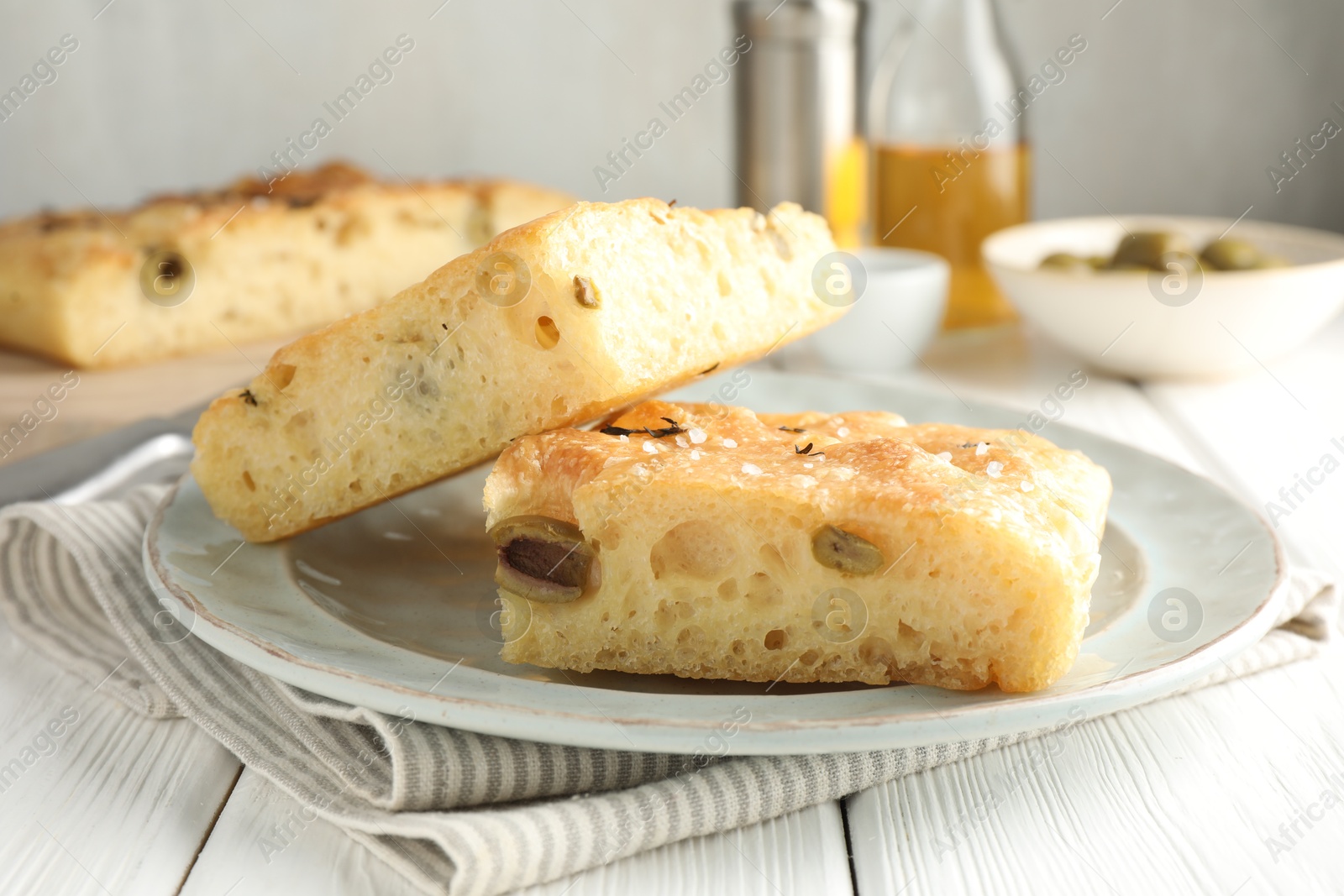 Photo of Pieces of delicious focaccia bread with olives, thyme and salt on white wooden table, closeup