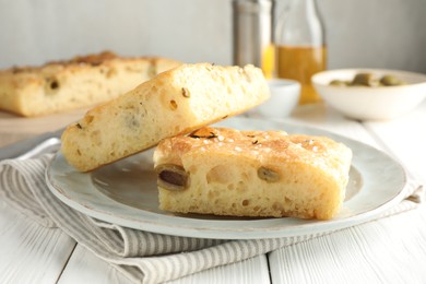 Photo of Pieces of delicious focaccia bread with olives, thyme and salt on white wooden table, closeup