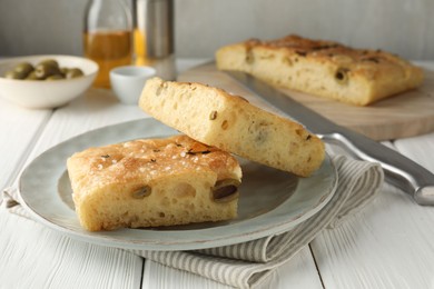 Photo of Pieces of delicious focaccia bread with olives, thyme, salt and knife on white wooden table, closeup