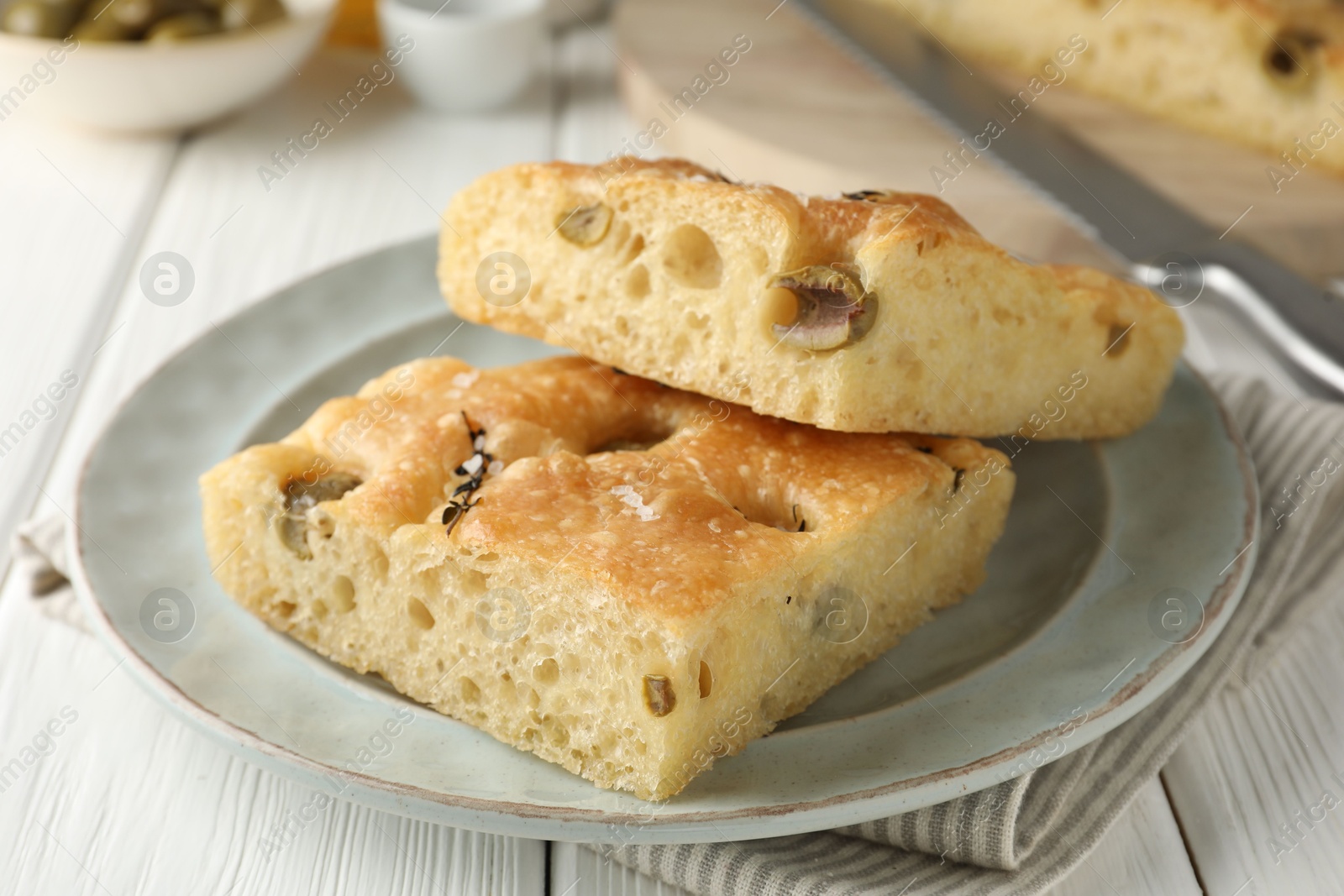 Photo of Pieces of delicious focaccia bread with olives, thyme and salt on white wooden table, closeup