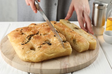 Photo of Woman cutting delicious focaccia bread at white wooden table, closeup