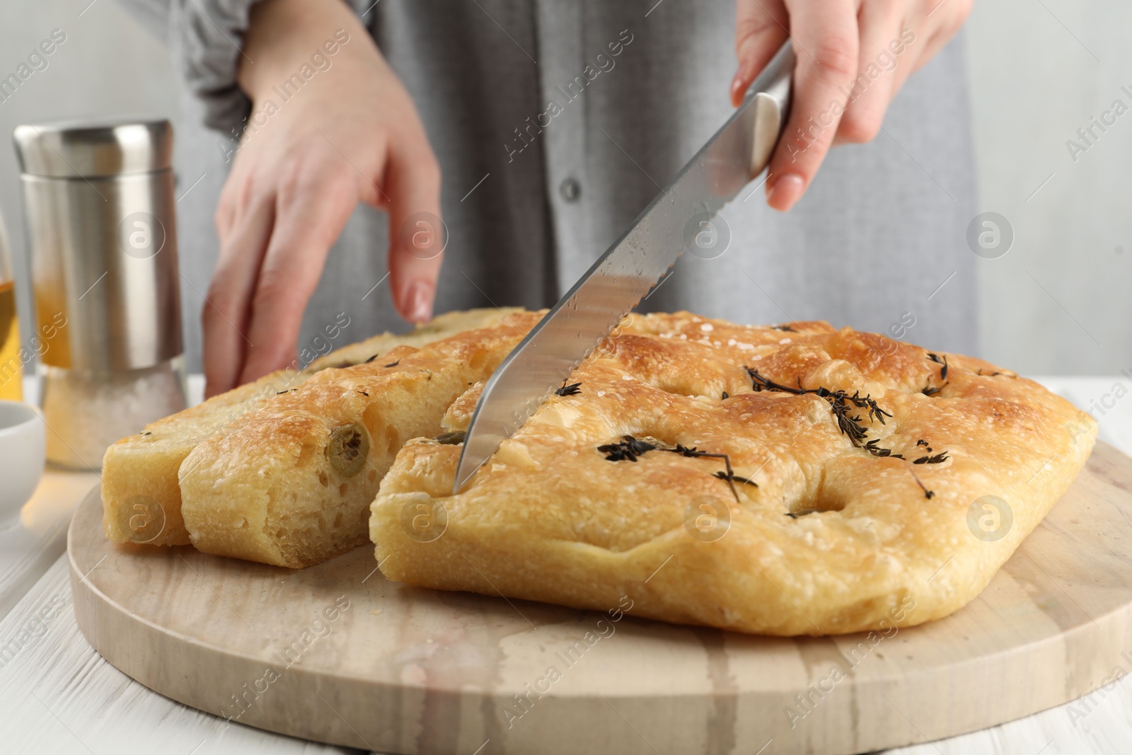 Photo of Woman cutting delicious focaccia bread at white wooden table, closeup