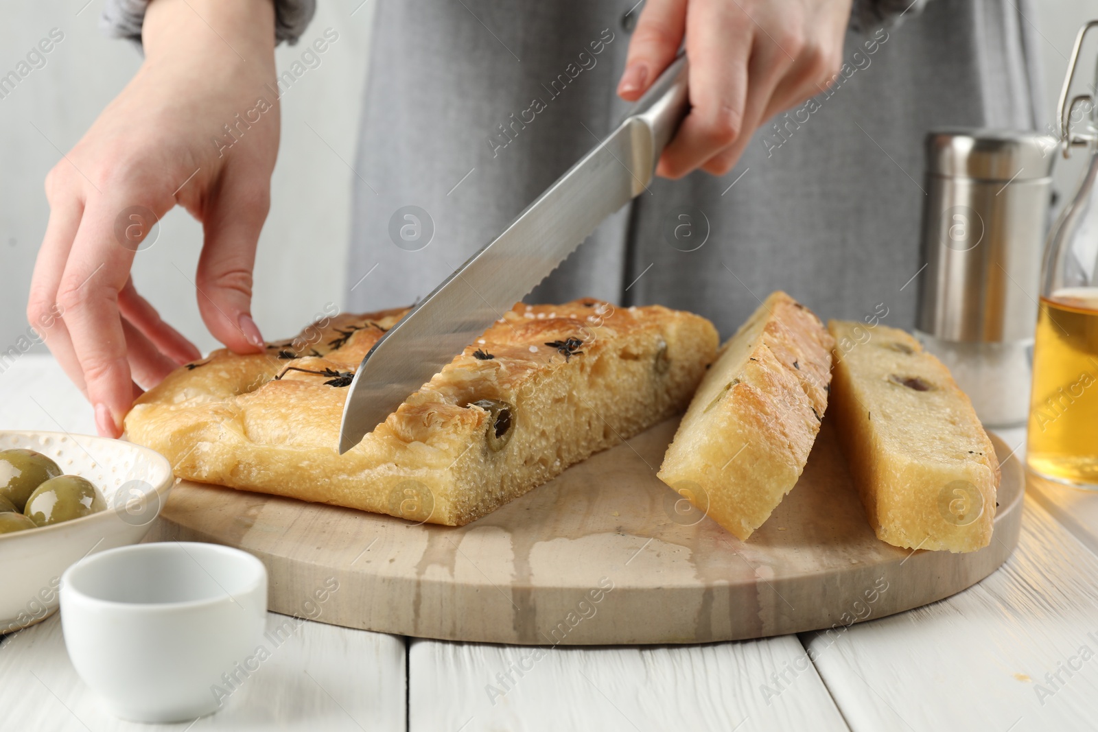 Photo of Woman cutting delicious focaccia bread at white wooden table, closeup