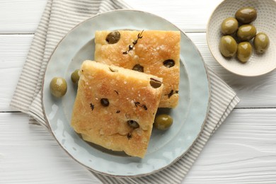 Photo of Slices of delicious focaccia bread with olives, thyme and salt on white wooden table, flat lay