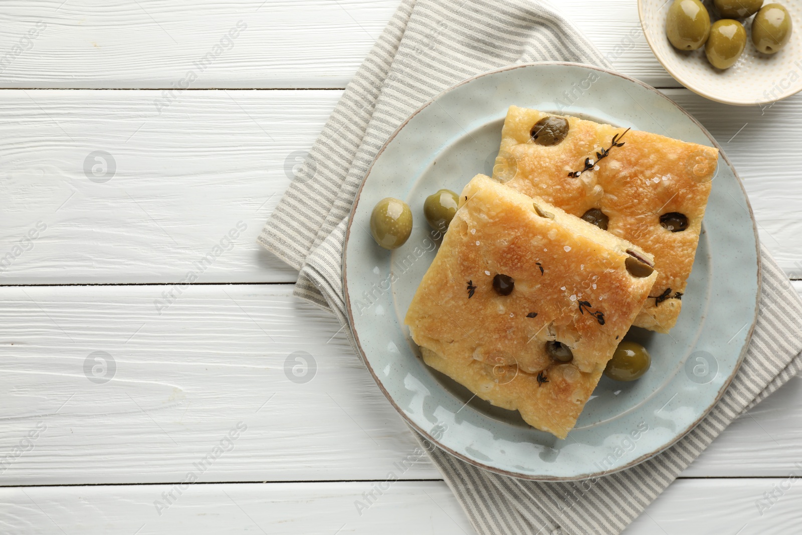 Photo of Slices of delicious focaccia bread with olives, thyme and salt on white wooden table, flat lay. Space for text