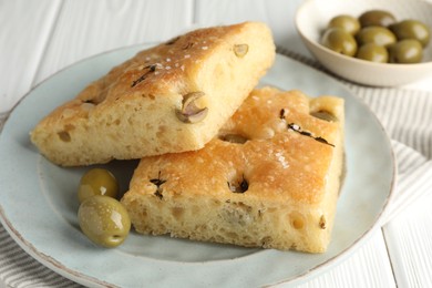 Photo of Slices of delicious focaccia bread with olives, thyme and salt on white wooden table, closeup