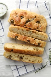 Photo of Slices of delicious focaccia bread with olives, thyme and salt on white wooden table, flat lay