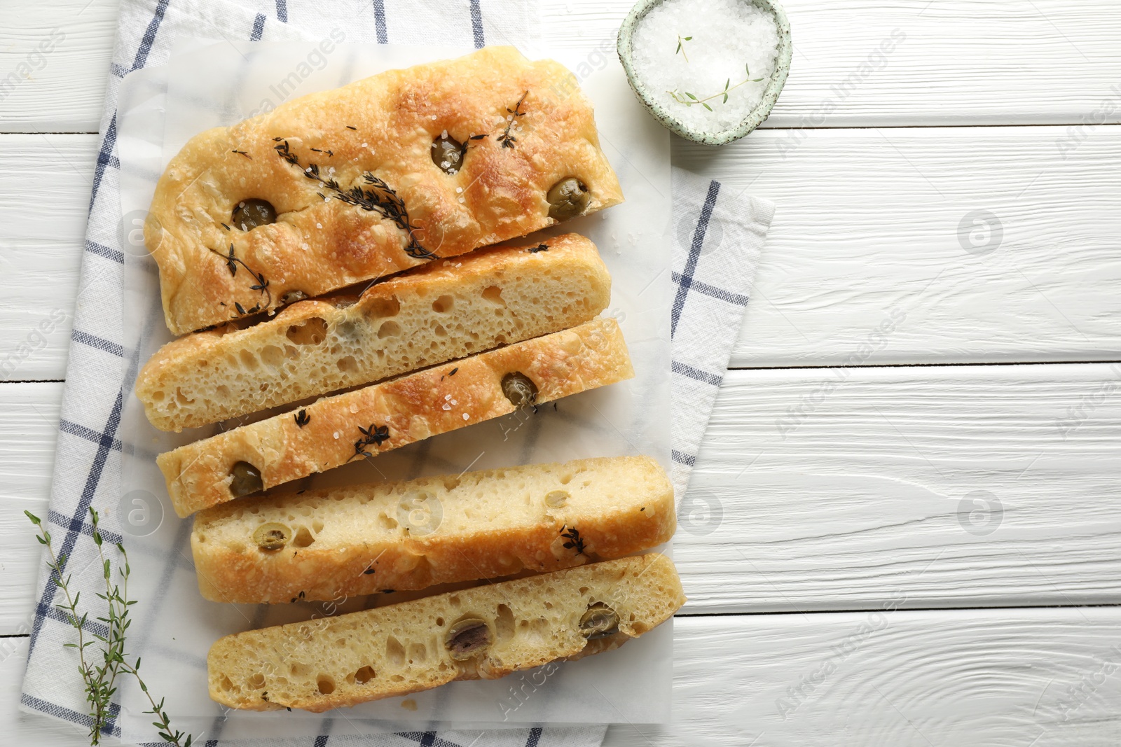 Photo of Slices of delicious focaccia bread with olives, thyme and salt on white wooden table, flat lay. Space for text