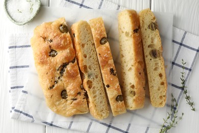 Photo of Slices of delicious focaccia bread with olives, thyme and salt on white wooden table, flat lay