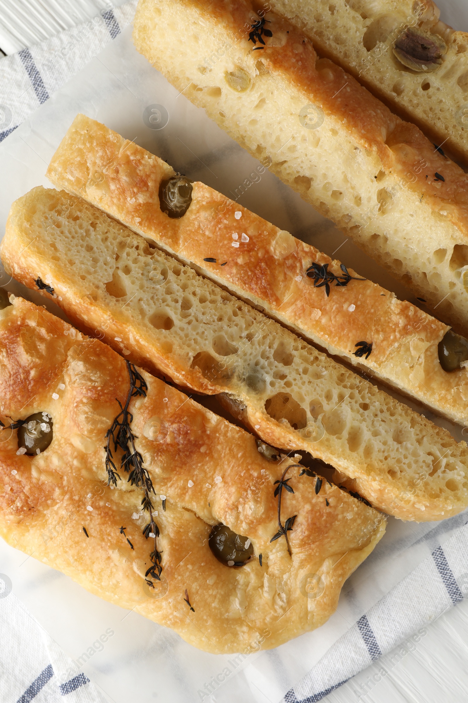 Photo of Slices of delicious focaccia bread with olives, thyme and salt on table, flat lay