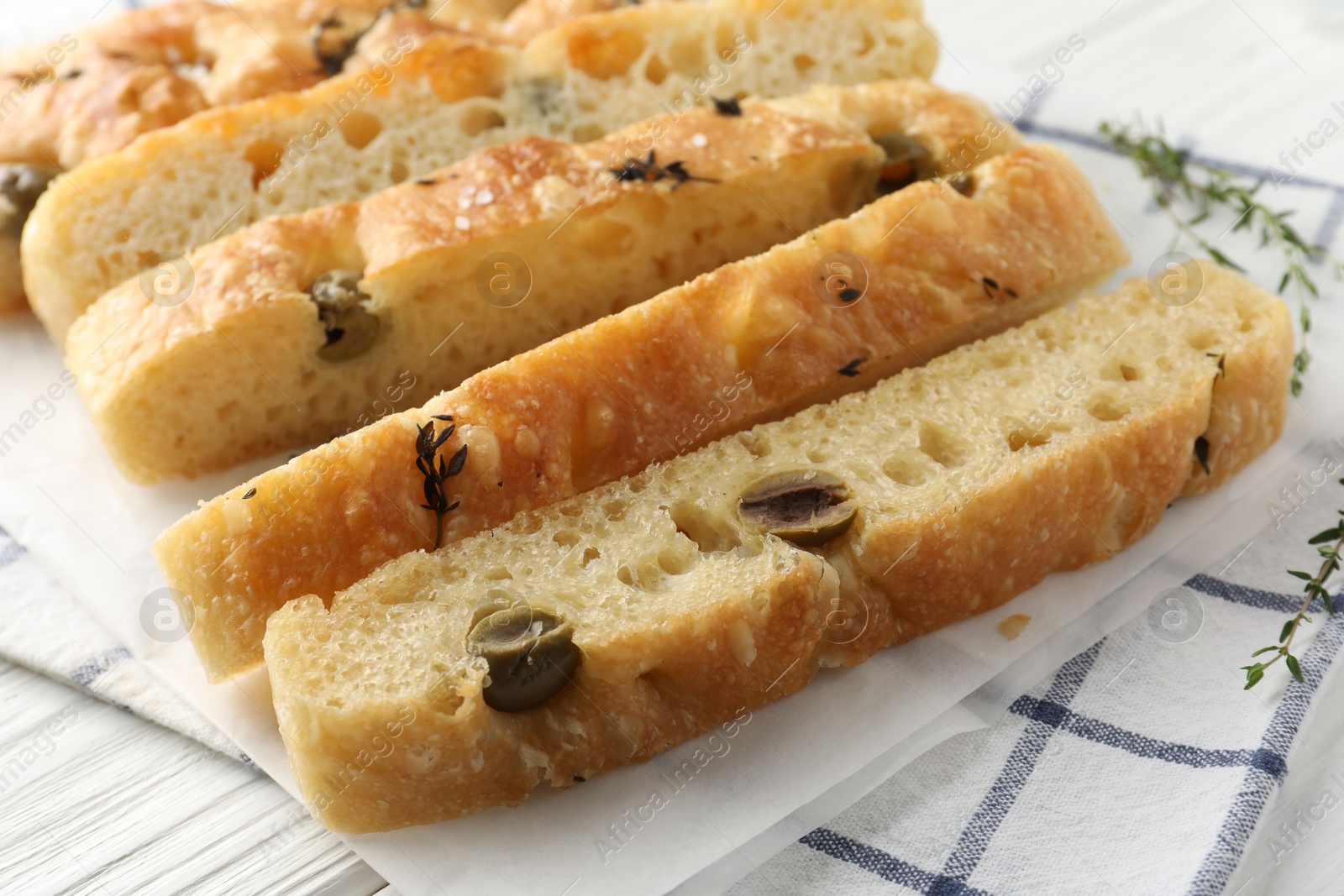 Photo of Slices of delicious focaccia bread with olives, thyme and salt on table, closeup