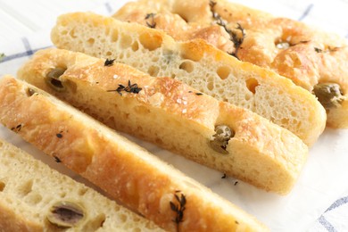 Photo of Slices of delicious focaccia bread with olives, thyme and salt on table, closeup