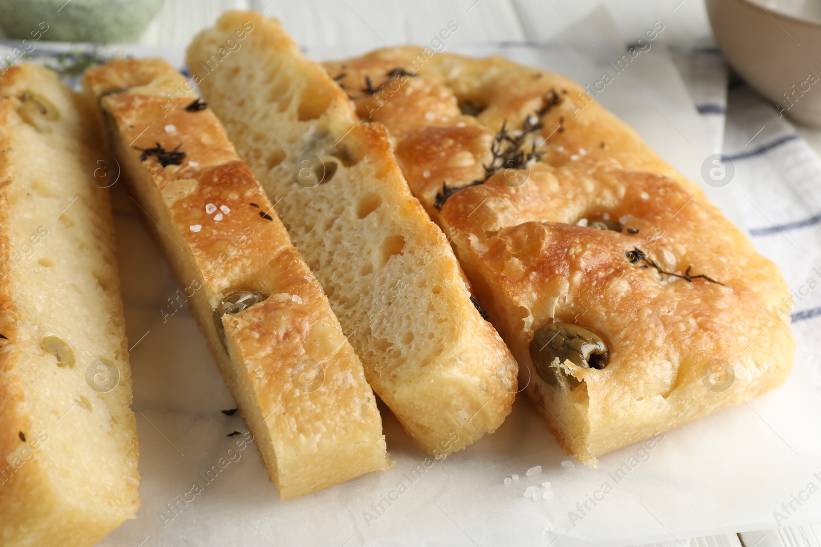 Photo of Slices of delicious focaccia bread with olives, thyme and salt on table, closeup