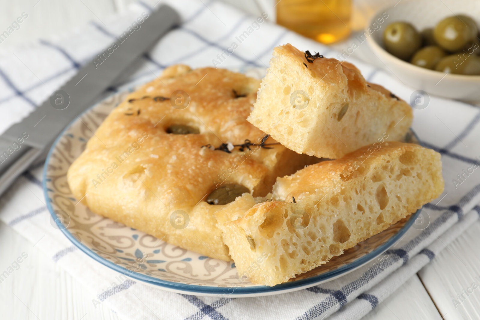 Photo of Slices of delicious focaccia bread with olives, thyme and salt on white wooden table, closeup