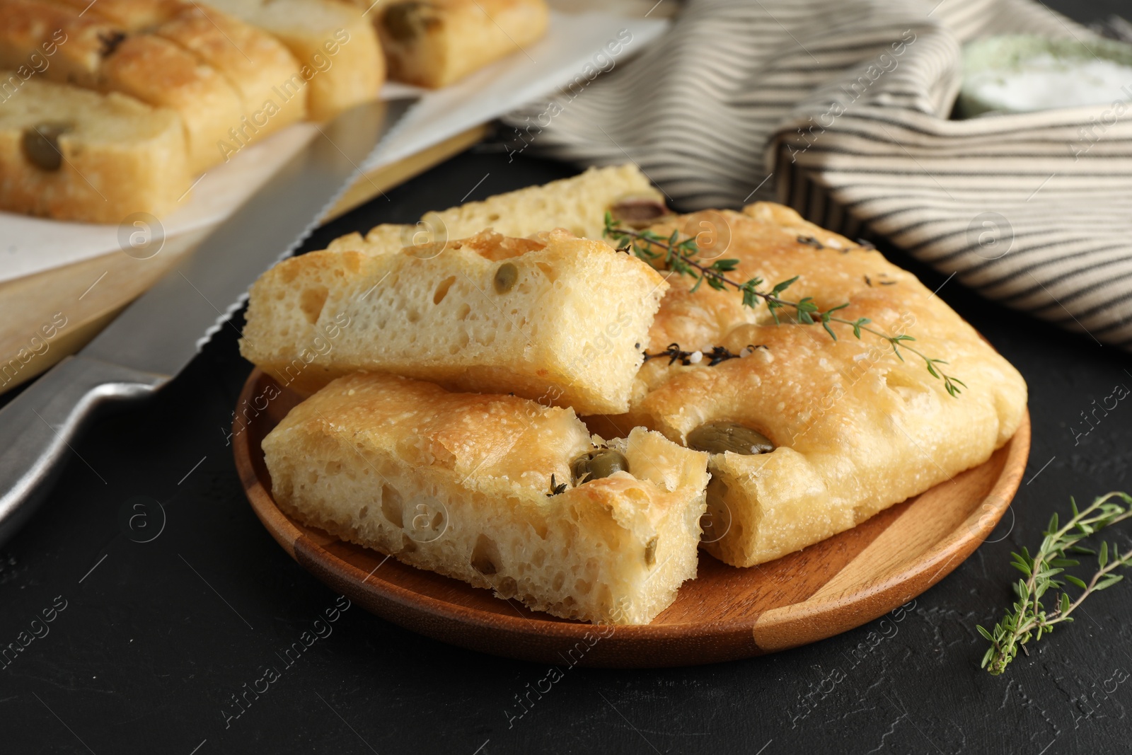 Photo of Slices of delicious focaccia bread with olives, thyme and salt on black table, closeup