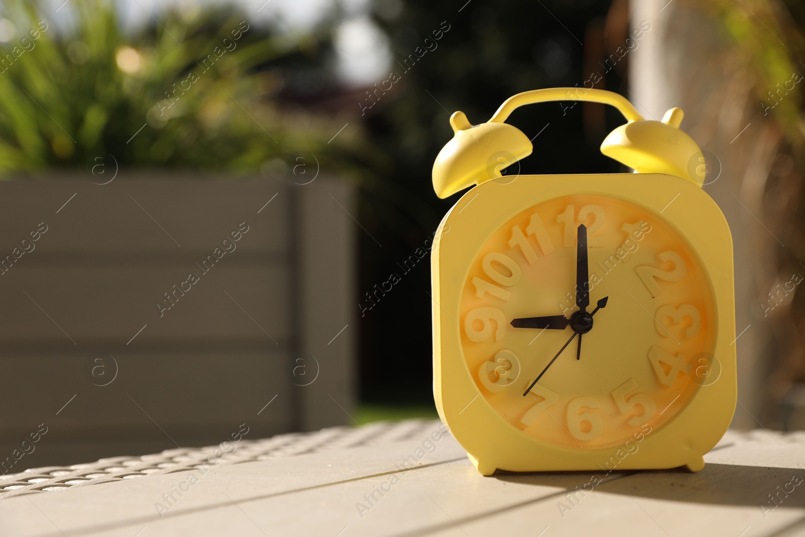 Photo of Yellow alarm clock on white wooden table outdoors at sunny morning. Space for text