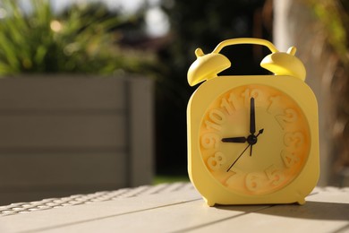 Photo of Yellow alarm clock on white wooden table outdoors at sunny morning. Space for text