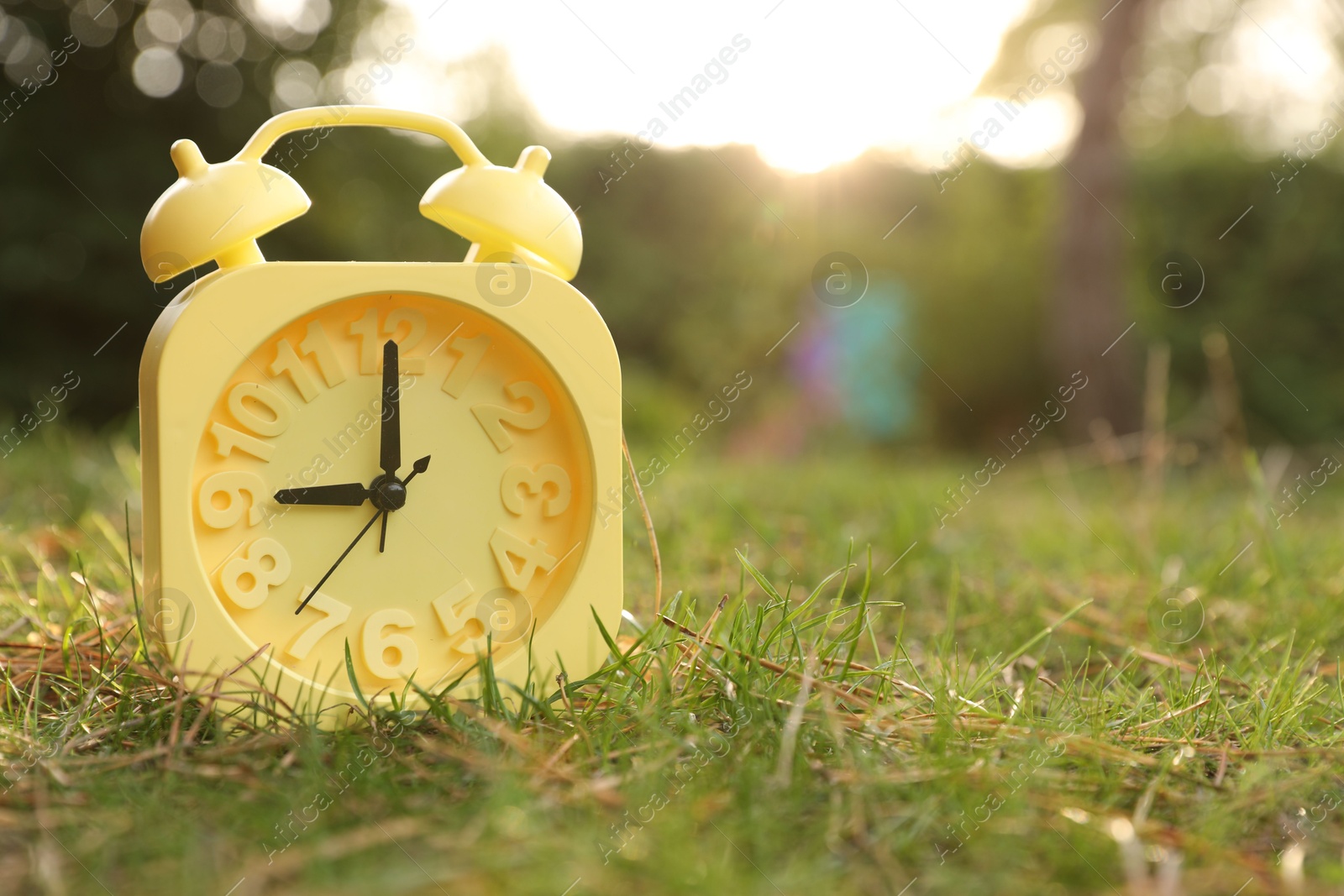 Photo of Yellow alarm clock on green grass outdoors. Space for text