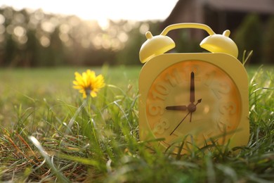 Photo of Yellow alarm clock on green grass outdoors. Space for text