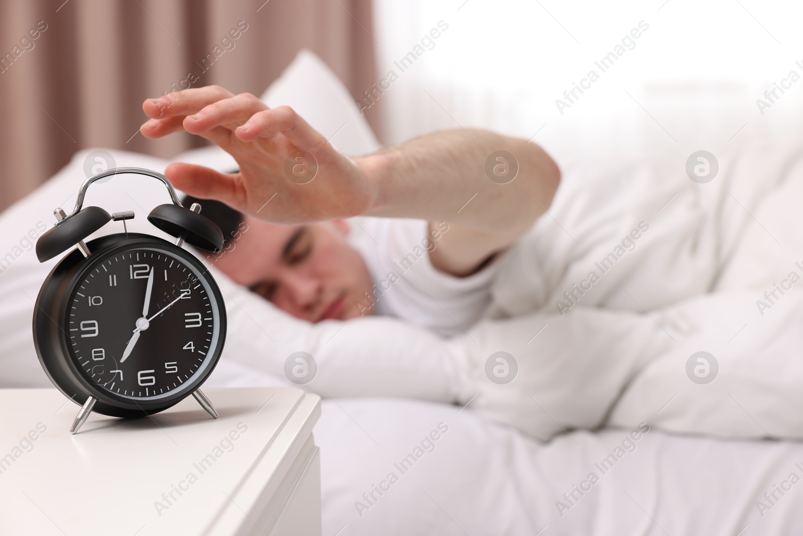 Photo of Man turning off alarm clock in bedroom, focus on hand. Space for text