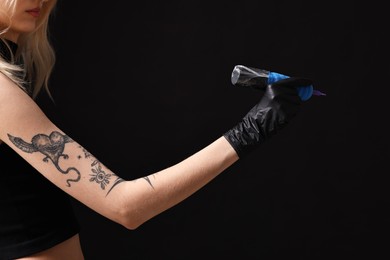 Photo of Professional artist in gloves holding tattoo machine on black background, closeup